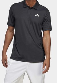 Černé polo tričko z prodyšné látky, s bílým logem ve tvaru tří pruhů na levé straně hrudi, klasickým límečkem a krátkými rukávy.