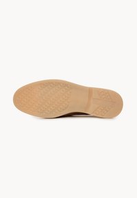Semelle en caoutchouc d'une chaussure beige avec motif de grip texturé et zone de support de voûte plantaire lisse, photographiée sur un fond blanc uni.