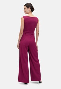 Fuchsia jumpsuit med vida ben, utan ärmar och figursydd midja. Har en dragkedja på ryggen och ett smidigt, lätt tyg.