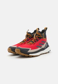 Höga trail-skor med en design i röd, svart och beige, texturerad överdel och en kontrasterande gummisul med uttalad sula för bra grepp.