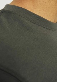 Dark green cotton t-shirt featuring a ribbed crew neckline and smooth texture. The focus is on the collar and shoulder area.