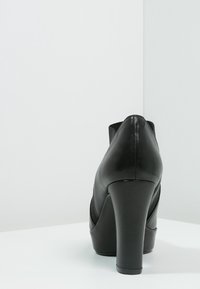 Chaussure à talon haut en cuir noir avec un bout arrondi et des panneaux latéraux texturés. Le talon est épais et courbé pour plus de stabilité.