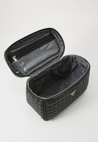 Borsa cosmetica nera imbottita con chiusura a zip, foderata in grigio e con tasca interna. Presenta una placca con il logo del marchio sul lato.
