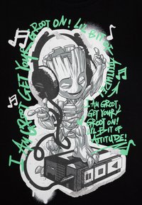 T-shirt noir avec un graphisme d'un personnage ayant une apparence d'arbre, portant des écouteurs, entouré de texte vert et de notes de musique.