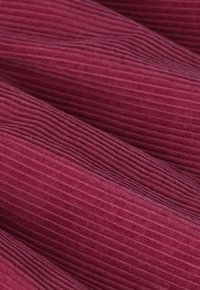 Un tissu en peluche plissé en velours côtelé rose foncé avec une texture rayée verticale distinctive à la surface.