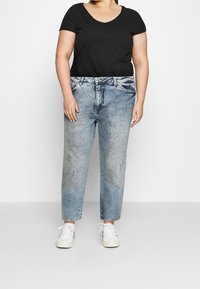 Schwarzes Kurzarmoberteil kombiniert mit hellblauen, geraden Jeans im faded Look mit subtilen Used-Effekten; weiße Sneakers.