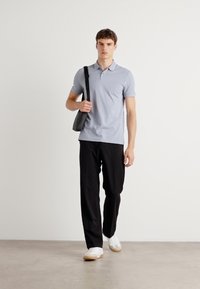 Camisa polo gris claro, pantalones negros y zapatillas blancas. La persona lleva un pequeño bolso negro de bandolera. Diseño sencillo, colores sólidos.