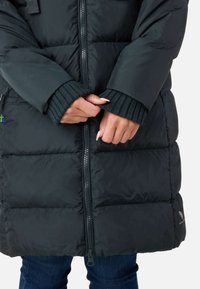 Sort pufjakke med fuld længde lynlås, ribbede manchetter og en tekstureret finish. Har en blå accent nær kanten og et logo.