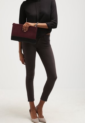 Svart kortärmad blus med en framdragning, mörkgrå smala jeans och en vinröd clutch med svart botten. Ljusgrå spetsiga klackar.