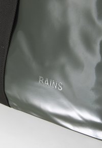 Vodootporna siva torba s glatkom teksturom i crnim remenom. Sadrži utisnuto ime branda 'RAINS' u srebrnoj boji.