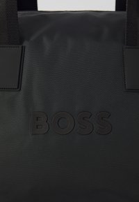 Geantă tote din nailon negru, cu logo embosat, textură netedă, mânere superioare duale și un design minimalistic.