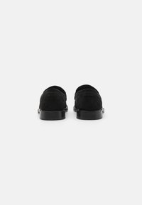 Mustad nahast loafers, millel on sile viimistlus, ümmargune varvas ja lame kummitald. Seljal on minimaalne bränding.