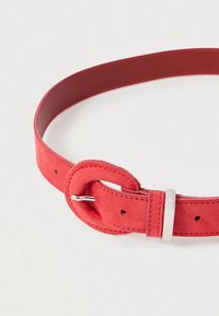 Curea din suede roșu cu un aspect neted, dotată cu o cataramă rotundă și un accent metalic. Include mai multe găuri de ajustare pe toată lungimea.