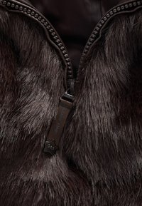 Gilet marrone in pelliccia sintetica con cerniera e linguetta in tessuto con la scritta "Sandy Liang." Interno liscio a contrasto con l'esterno strutturato.