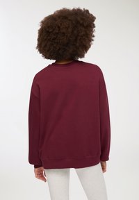 Felpa bordeaux con design rilassato, scollatura a costine e maniche lunghe. Realizzata in tessuto morbido; presenta un motivo semplice e uniforme.