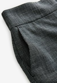 Grå mønstret stof med en tekstureret overflade, der har et ternet design. Stoffet har en skræddersyet kant og en ren, struktureret fold.