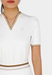 Witte polo jurk met een V-hals, korte pofmouwen en gouden accentstrepen. Heeft een subtiele logo op de borst en een gestructureerde tailleband.