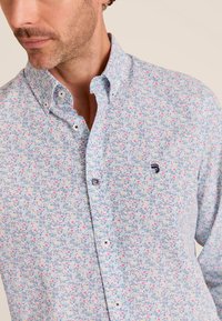 Lichtblauwe bloemenblouse met kleine roze en gele bloemen, een puntkraag en witte knopen met een marine accent.