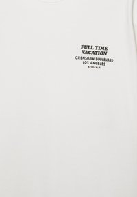 Cămașă albă cu text negru pe piept cu inscripția „FULL TIME VACATION Crenshaw Boulevard Los Angeles 3773 Calif.”
