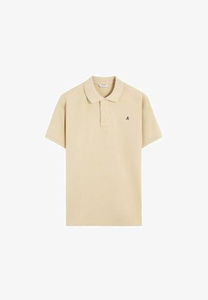 Polo de manga corta beige con cuello, tapeta de dos botones y pequeño logo de calavera negra en el pecho izquierdo.
