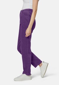 Pantaloni in corduroy viola con taglio dritto, dotati di tasche frontali e una finitura testurizzata, abbinati a sneaker bianche.