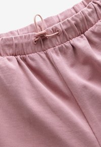 Bløde pink stof joggere med elastisk talje og snørrebånd samt indsamlet tekstur, der fremhæver et glat og åndbart materiale.