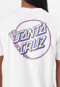 White cotton t-shirt displaying a graphic with "SANTA CRUZ" in bold yellow and purple letters, featuring a UFO and alien design.