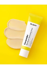 Crème hydratante pour la barrière cutanée Ceramidin de Dr. Jart+ dans un tube blanc avec des accents jaunes ; échantillons de crème sur un fond jaune vif.