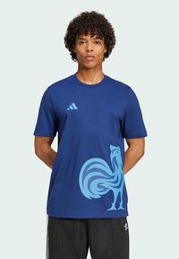 Marineblauwe katoenen T-shirt met een grote lichtblauwe haanafbeelding op de voorkant en drie witte strepen op de linkerschouder.
