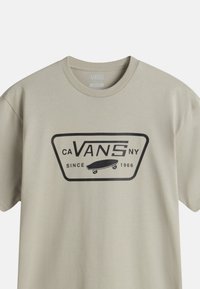 Camiseta de algodón beige con un logo gráfico negro que presenta un diseño de patineta y el texto "CA VANS NY DESDE 1966" en letras negritas. Mangas cortas.