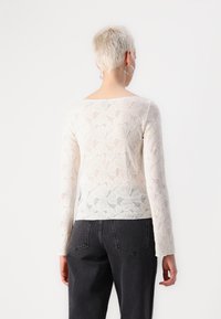 White lace long-sleeve top featuring a floral pattern and a scoop back, paired with high-waisted black jeans. Smooth texture and lightweight design.