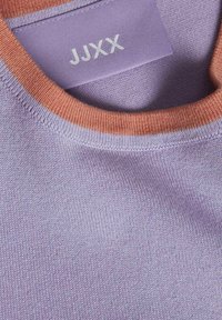 Telaje de punto morado con un cuello naranja en contraste. Una etiqueta cosida muestra "JJXX" en texto blanco en el interior del cuello.