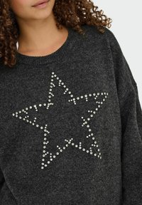 Pull gris en matériau doux, avec un décolleté large et un motif étoile en strass sur le devant.
