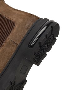 Stivaletto in camoscio marrone con un pannello in tessuto a coste, suola in gomma nera e un motivo del battistrada testurizzato. Punta arrotondata e accenti minimali.