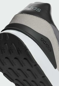 Gros plan du talon d'une chaussure de sport Adidas grise et noire avec une semelle texturée noire et le logo Adidas sur le côté et à l'arrière.