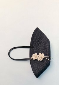 Borsa a tracolla nera intrecciata con due manici neri, caratterizzata da una superficie testurizzata e due decorazioni floreali crema vicino alla base.