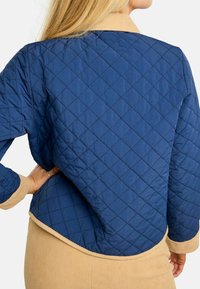 Granatowa pikowana kurtka w diamentowy wzór; posiada beżowy kołnierz i obszycie, wykonana z teksturowanego, lekkiego materiału.