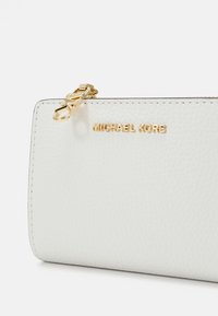 Balta teksturēta ādas maks ar zelta Michael Kors logotipu un zelta rāvējslēdzēja vilkšanas cilpu sānos.
