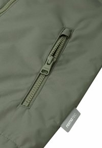 Giacca verde con tasca con zip e superficie texturizzata. Include un'etichetta piccola con il testo "reima TEC."