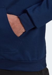 Sweatshirt bleu marine avec une poche kangourou, des poignets côtelés et une texture lisse. Les coutures et les assemblages sont bien définis et renforcés.