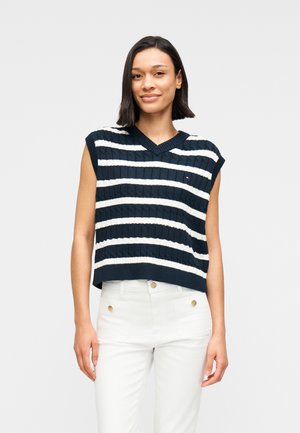 Pull tricoté bleu marine court avec des rayures horizontales blanches, doté d'un col en V et de manches courtes. Associé à un pantalon blanc.