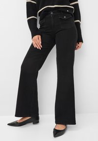 Jeans neri a zampa d'elefante con vita alta, dotati di tasche frontali e posteriori, chiusura con bottone in metallo e una texture denim morbida. Abbinati a ballerine nere.