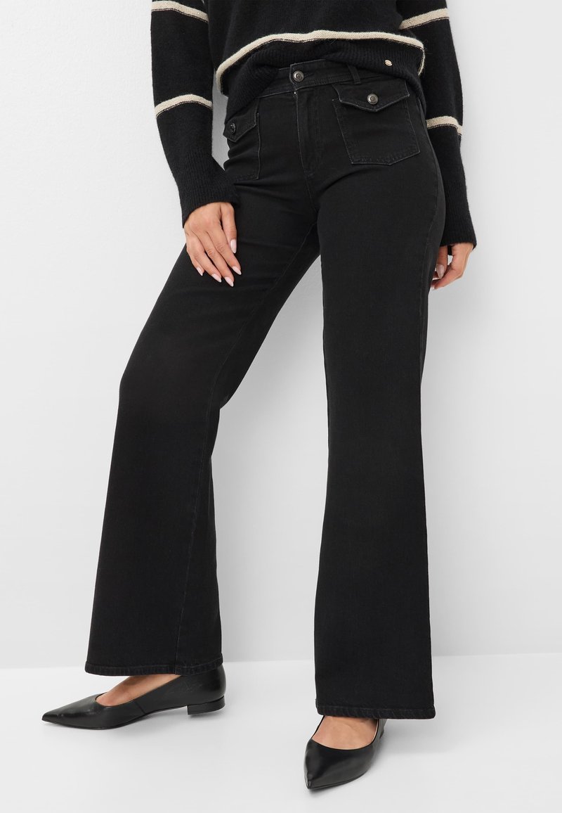 Jeans neri a zampa d'elefante con vita alta, dotati di tasche frontali e posteriori, chiusura con bottone in metallo e una texture denim morbida. Abbinati a ballerine nere.