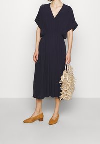 Mørkeblå midi-kjole med V-hals og korte ærmer, samlet ved taljen. Styling med beige vævede blokhælede sko og en tekstureret beige taske.