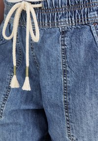 Svetlo modri jeans kratki hlače z elastičnim pasom, ki imajo pleteno krema vrvico zavezano spredaj, okrašeno z resicami na koncih.