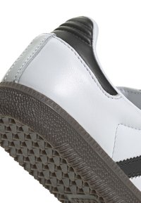 Vit lädersneaker med svarta accenter. Texturerad gummisula med triangulära mönster. Slät yta med kontrasterande sömdetaljer.