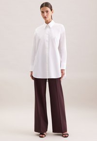 Camicia bianca a maniche lunghe con colletto a punta, abbinata a pantaloni larghi bordeaux. Tessuto liscio con una vestibilità comoda.