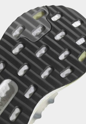 Primer plano de la suela de zapato negra con secciones de agarre blancas texturizadas y crestas horizontales sobre un fondo claro.