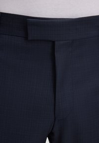 Nahaufnahme der Taille einer marineblauen maßgeschneiderten Hose mit verborgenem Haken- und Ösenverschluss und strukturiertem Stoffmuster.