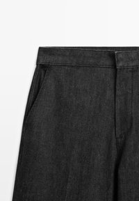 Zwarte spijkerbroek taille met voorzak en riemlussen op een witte achtergrond.
